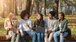 © Prostock-studio - Joyful multiracial teen friends having conversation and using gadgets while resting in park