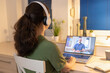 © _KUBE_ - Back view of young woman working at laptop and wearing headphones. Freelance and online education. Remote video consultation with psychotherapist