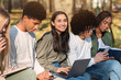 © Prostock-studio - Multiracial teen friends spending time outdoors, using gadgets and reading books at park