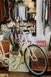 © AnnaStills - Bicycles, a backpack, and shelves full of clothing and accessories seen in cozy thrift store interior with an organized, eclectic mix of items and sale signage visible