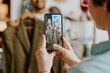 © AnnaStills - Person holding smartphone capturing video of another individual holding brown jacket in a store setting focusing on the clothing item