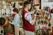 © AnnaStills - Two people browsing inside vintage clothing store, examining various garments and accessories while surrounded by eclectic decor and an assortment of items