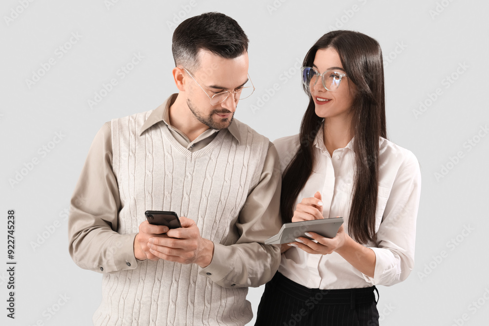Young couple in eyeglasses with mobile phone and calculator on light background