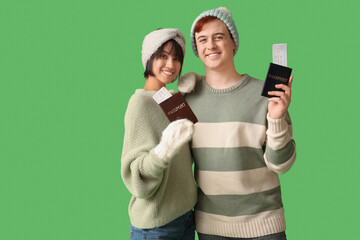 Beautiful young happy couple with passports and tickets on green background. Winter vacation concept