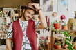 © AnnaStills - Man adjusting hat in cozy boutique surrounded by vibrant plants, stylish accessories, and charming decor creating a warm and inviting atmosphere