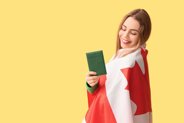 Wall Mural - Beautiful young happy woman with Canadian flag and passport on yellow background