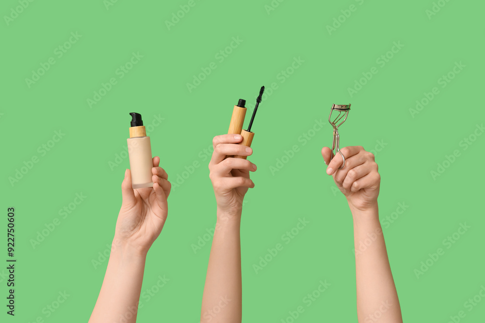 Female hands with foundation, eyelashes curler and mascara on green background