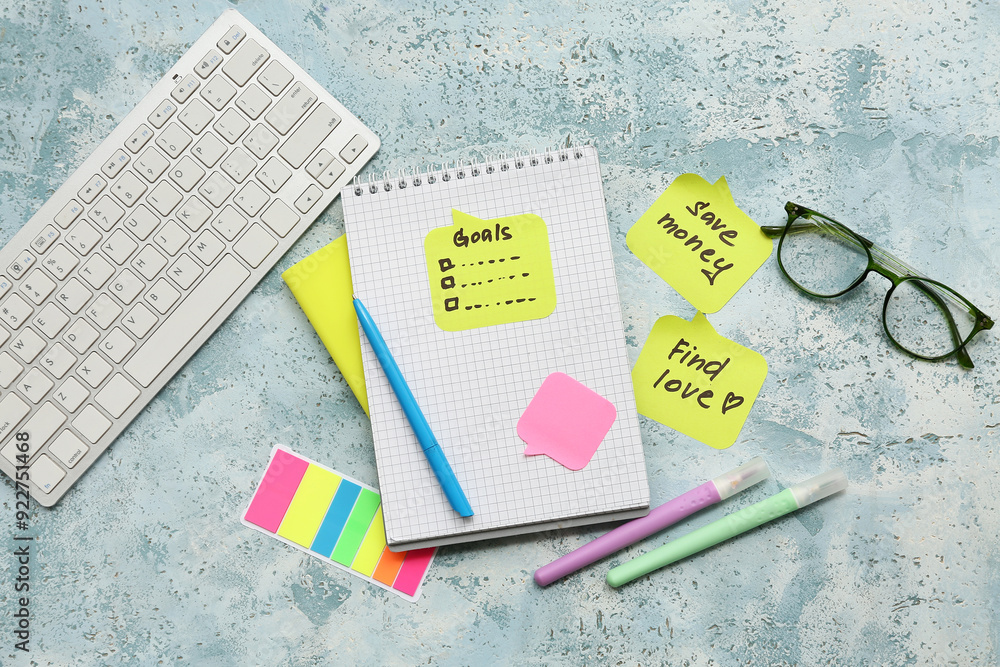 Sticky notes with to do plans, computer keyboard and notebook on blue grunge background. New year goals concept