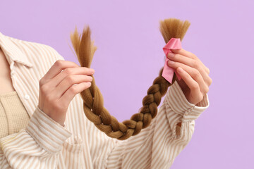 Wall Mural - Female hands with braided red hair for donation and pink awareness ribbon on purple background