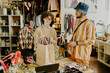 © AnnaStills - Smiling shopkeeper packing clothes for customer in clothing shop, both engaged in friendly conversation. Shelves with merchandise in background create a cozy atmosphere