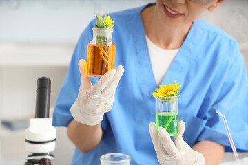 Happy female scientist with flasks of samples, microscope and sunflowers working in laboratory, closeup