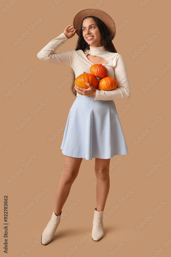 Stylish young woman with fresh pumpkins on brown background