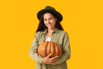 Wall Mural - Stylish young woman with fresh pumpkin on yellow background