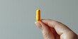 © AMA STUDIO - Hand holding a single yellow pill on neutral background