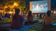 © Prostock-studio - A crowd sits on blankets in a park, watching a film projected onto a large screen while enjoying the warm evening atmosphere.