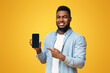 © Prostock-studio - Handsome african american guy demonstrating smartphone with black screen and pointing on it, yellow background with free space