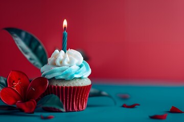 Cupcake with lit candle and red flowers on blue surface