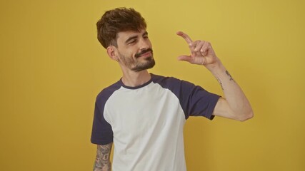 Sticker - Confident young hispanic man gesturing small size sign with fingers, standing over isolated yellow background