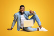 © Prostock-studio - Freelance work concept. Happy black guy sitting on floor with laptop and showing thumb up and looking at camera on yellow background