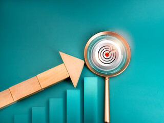 Business growth, development, success goal and leadership concept. Big target icon in magnifying glass lens with wood arrow blocks on growth graph diagram on blue background, minimal and eco style.