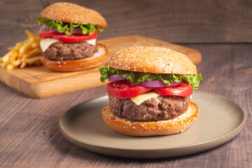 Homemade delicious hamburger with beef, onion, tomato, lettuce and cheese. Fresh burger close up on wooden rustic table with potato fries. Cheeseburger. Burger.