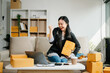 © Nuttapong punna - Young businesswoman managing online sales and shipping from a modern home office.
