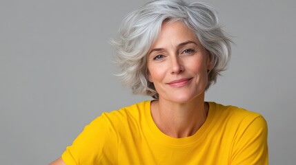 Wall Mural - mature woman with white skin, grey short hair, wavy hair and a clear yellow t shirt, isolated in a light grey studio