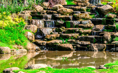 Selective focus of the flow of river water terraces or swale made of rocks near the river so that it looks like a small waterfall during the day.