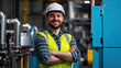 © britaseifert - A handsome male worker wearing a safety helmet and yellow vest is standing in front of the machines with his arms crossed
