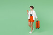 © ViDi Studio - Full body happy fun traveler woman wearing casual clothes hold suitcase bag use mobile cell phone isolated on plain green background. Tourist travel abroad in free time rest. Air flight trip concept.