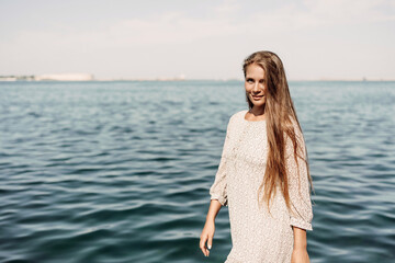 Canvas Print - A woman is walking on the beach wearing a dress. The water is calm and the sky is clear.