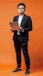 © Denisa - A young man in formal attire stands confidently, holding a tablet in a vibrant orange environment