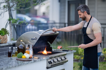 Poster - Portrait of a cheerful young man grilling meat on barbecue outdoors.. Roasting and grilling food. Roasting meat outdoors. Barbecue and grill. Cooking meat in backyard.