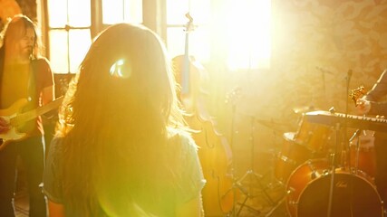 Wall Mural - A woman with long hair stands in front of a group of musicians. Scene is energetic and lively, as the woman is a part of a band or a music group