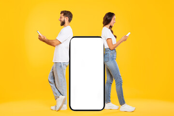 Mobile offer concept. Young man and woman using smartphones, leaning on huge cellphone with blank white screen, yellow background