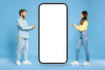 European man and woman walking to huge cellphone with blank white screen and using their phones, smiling to each other, mockup
