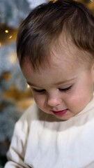 Wall Mural - Pretty little kid sits over a decoration for Christmas tree. Adorable child enjoys the toy and waves hands excitedly.