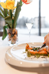 cute girl is eating a delicious dish with juicy salmon, fresh vegetables, avocado, and fragrant herbs, served on a beautiful white plate on a wooden table in a cozy, charming restaurant