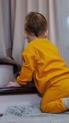 Poster - Lovely toddler in orange sport suit sits on the floor near the stairs. Kid throws the toy and watches it roll.