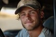 © Milos - A young man with a rugged look, wearing a cap inside his vehicle, smiles contentedly at the camera, conveying a sense of ease and rugged outdoorsy charm.