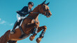 © BetterPhoto - Focused male equestrian riding a brown horse mid-jump against a clear blue sky, demonstrating precision and strength in equestrian sports.