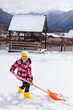 © Studio Peace - Happy little girl cleans snow with a big shovel against the background of mountains.