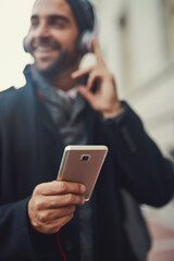 Wall Mural - Hand, phone and man listening to music, podcast and jazz to travel on work commute to city in winter. Mobile, headphones and happy person closeup outdoor streaming audio, sound and radio app online