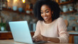 © aekkorn - Happy black woman using laptop in the kitchen.