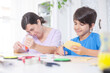 © OR MIXphoto - Smiling mother and son sitting side by side at a desk where they do handicrafts.