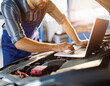© Iqy - A mechanic uses a laptop to diagnose and repair a car engine in a sunlit workshop.