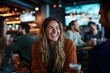 © Milos - A woman with long hair laughs heartily while enjoying a drink with friends in a lively bar, capturing the essence of fun, friendship, and social joy.
