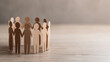 © tonstock - Paper cutout figures holding hands in a circle, representing unity and teamwork on a wooden background.