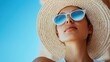 © Dulemegapixel - Close-up image of a woman wearing a straw hat looking up at the sky, with a background of clear blue sky, capturing a peaceful and relaxed moment outdoors.