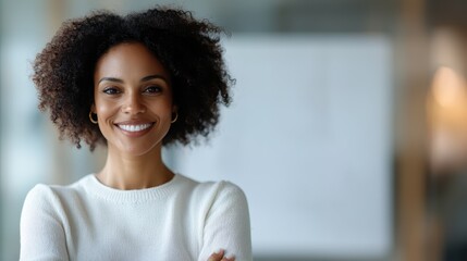 A professional woman with curly hair, stands confidently with a smile in a bright modern room, embodying joy and success along with a welcoming, positive atmosphere.